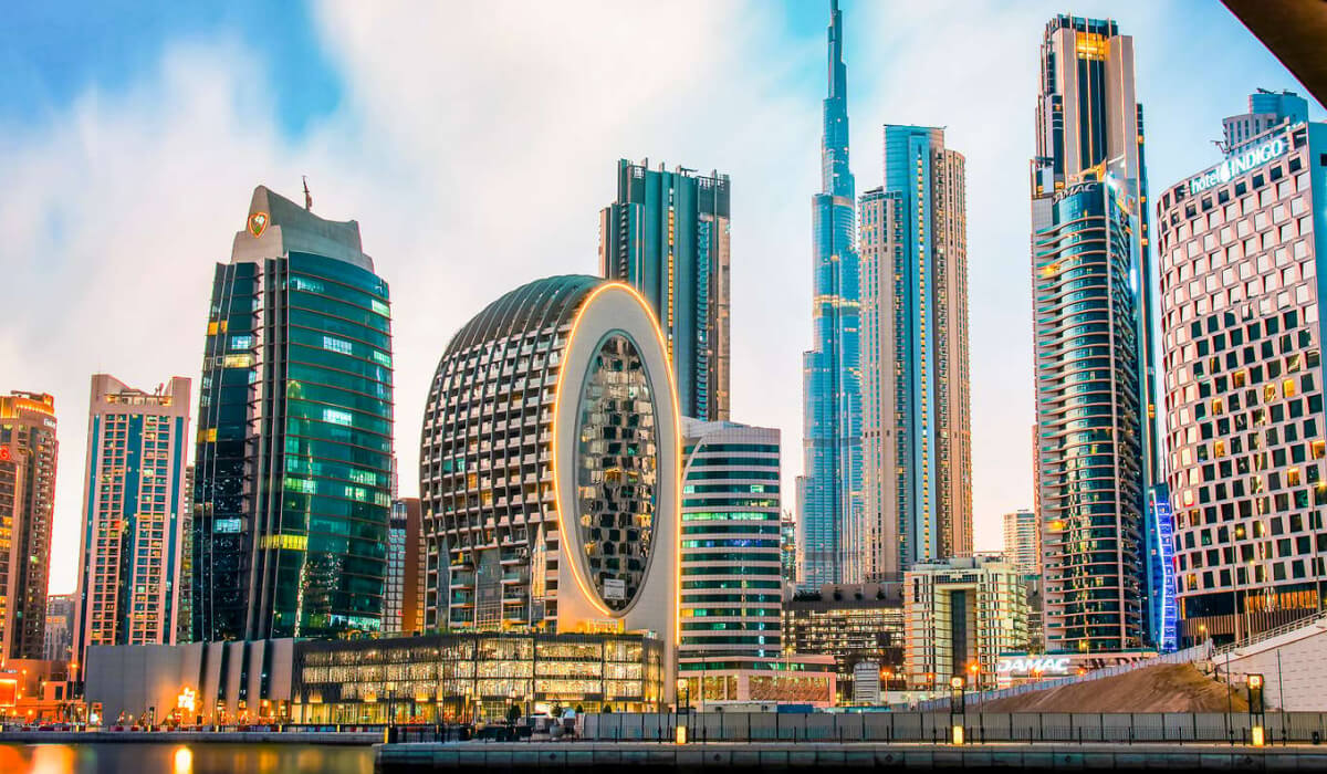 Business Bay area with towering skyscrapers, modern architecture, and numerous office windows, illuminated brightly against a blue skyline.