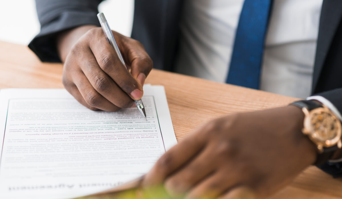 A person in a suit is signing a document, with a close-up of their hand wearing a stylish watch, highlighting the formality and professionalism of the moment.