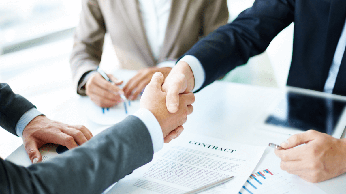 Three businesspeople shake hands near a table with a contract, symbolizing the successful completion of an agreement in a professional setting.