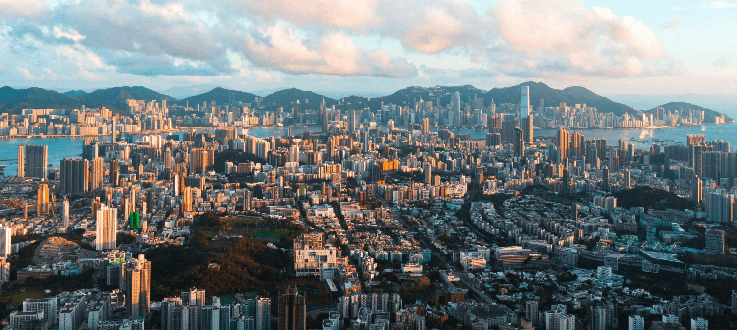 A top view of Hong Kong showcasing a mix of modern skyscrapers, greenery, and water, with a bright sky and an endless horizon stretching into the distance, highlighting the city's vibrant blend of nature and urban development.