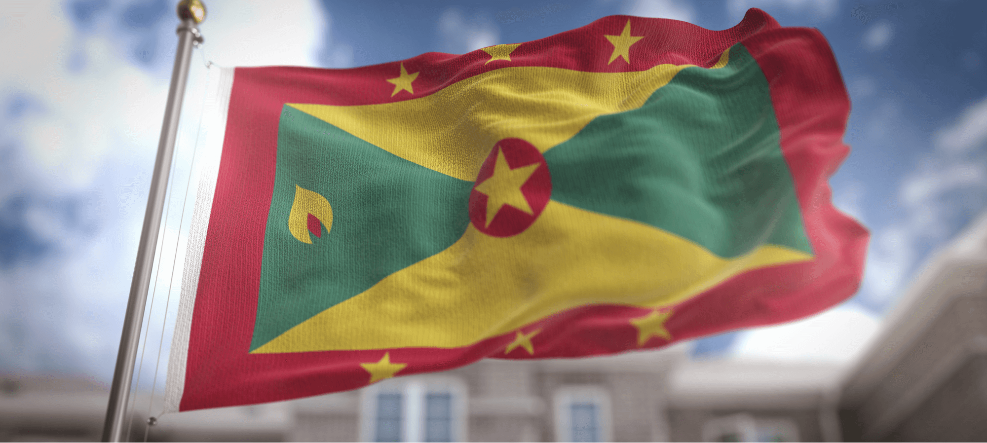 A large Grenada flag waves proudly against a bright, clear sky, showcasing its vibrant colors.