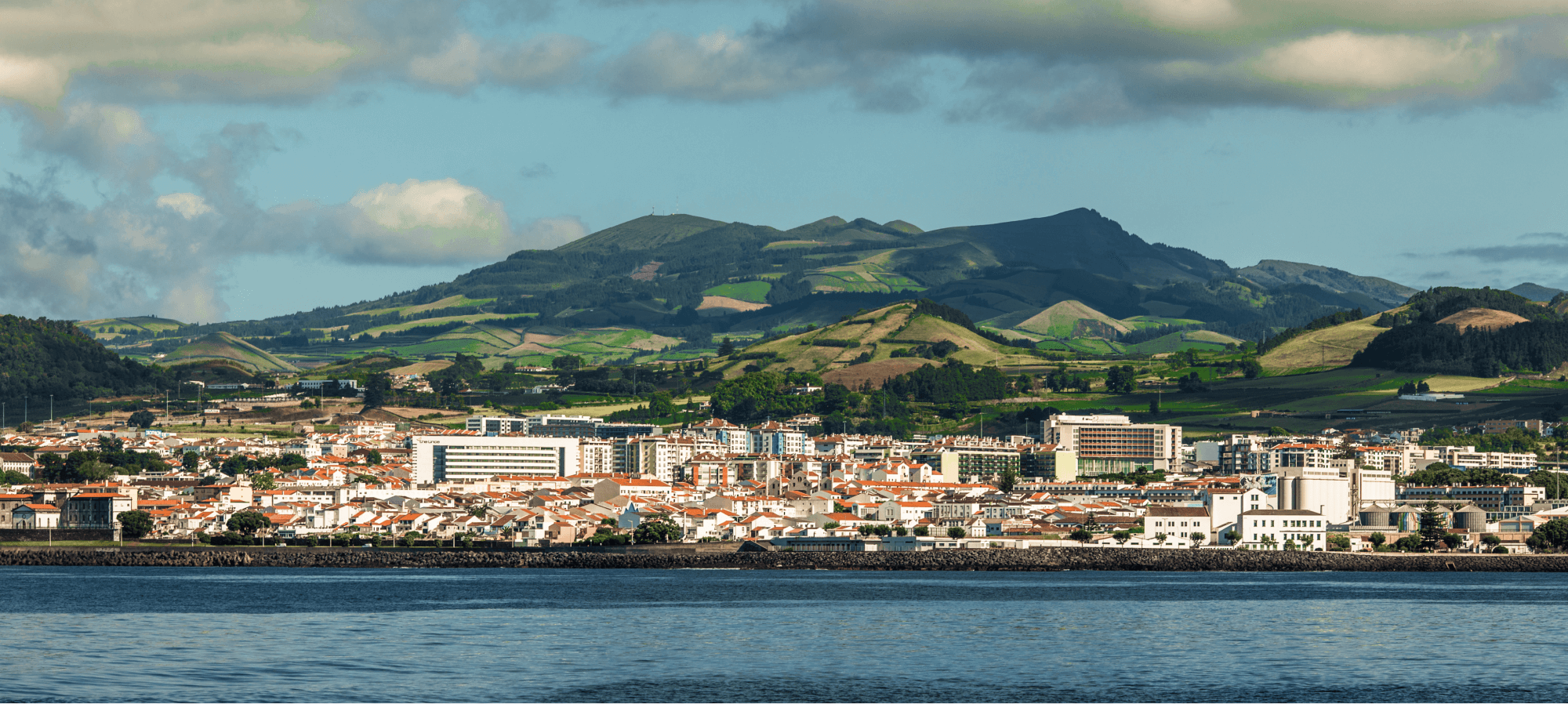 A scenic view of a green mountain in Grenada, with a charming small city nestled in front, all under a bright sky, creating a cozy and inviting atmosphere.