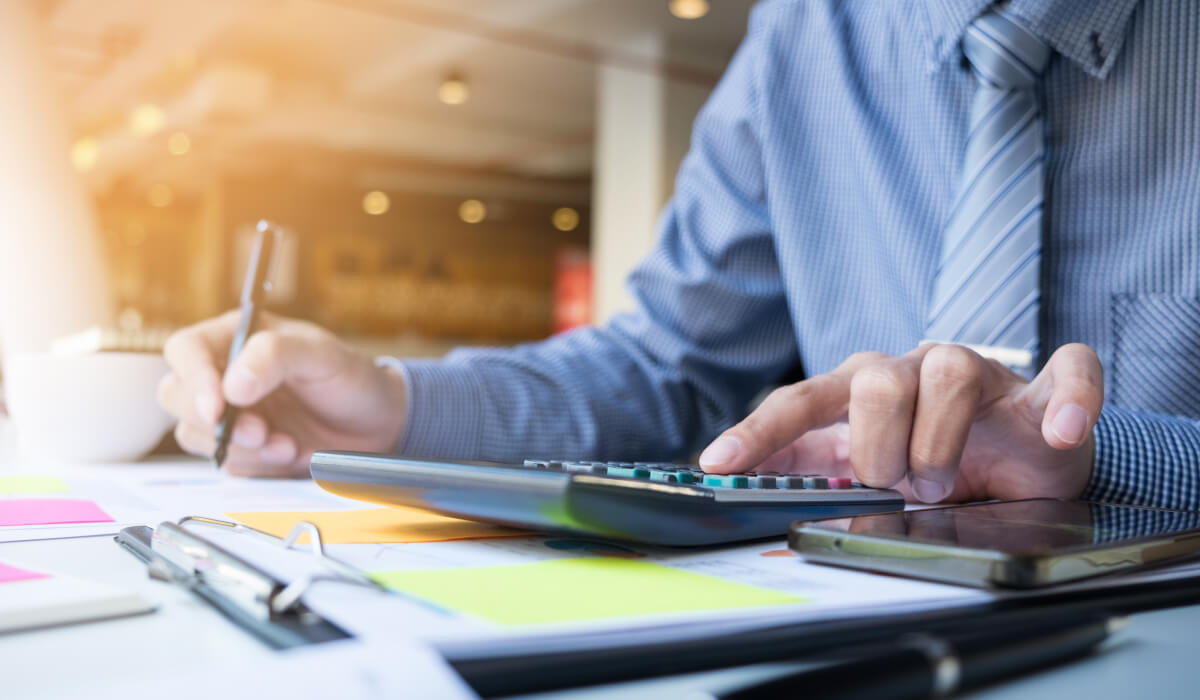 A professional in a suit working on documents at a desk, with a calculator placed nearby.