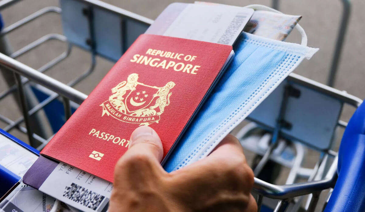 A hand holding a Singaporean passport with a flight ticket and a COVID mask, symbolizing travel readiness and safety in a modern global context.