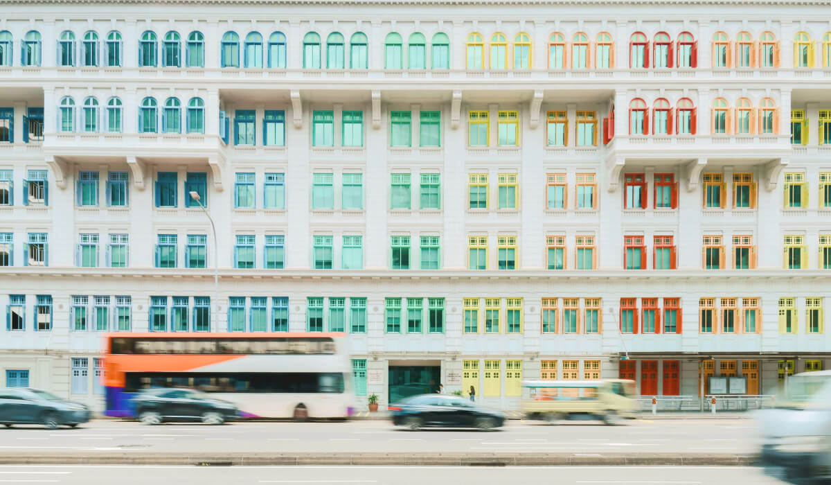 Vibrant Singapore building with colorful blue, yellow, green, and orange windows, with blurred vehicles passing in front, capturing the city's dynamic energy.