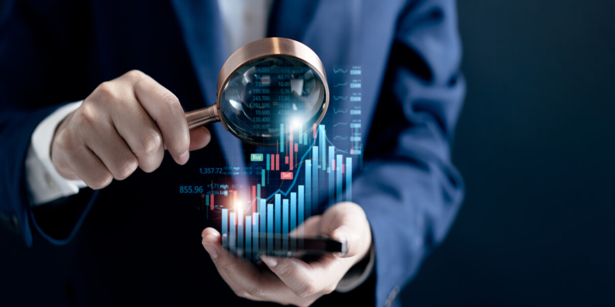 A man in a suit holds a zoom lens over a phone screen, showcasing rising charts and numbers that symbolize financial growth and success.