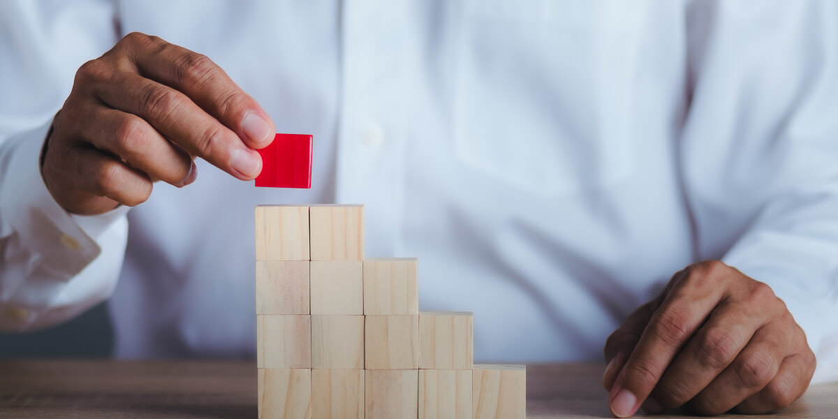  A man in a white shirt stacks small light brown cubes, carefully placing a red cube on top as the final piece.