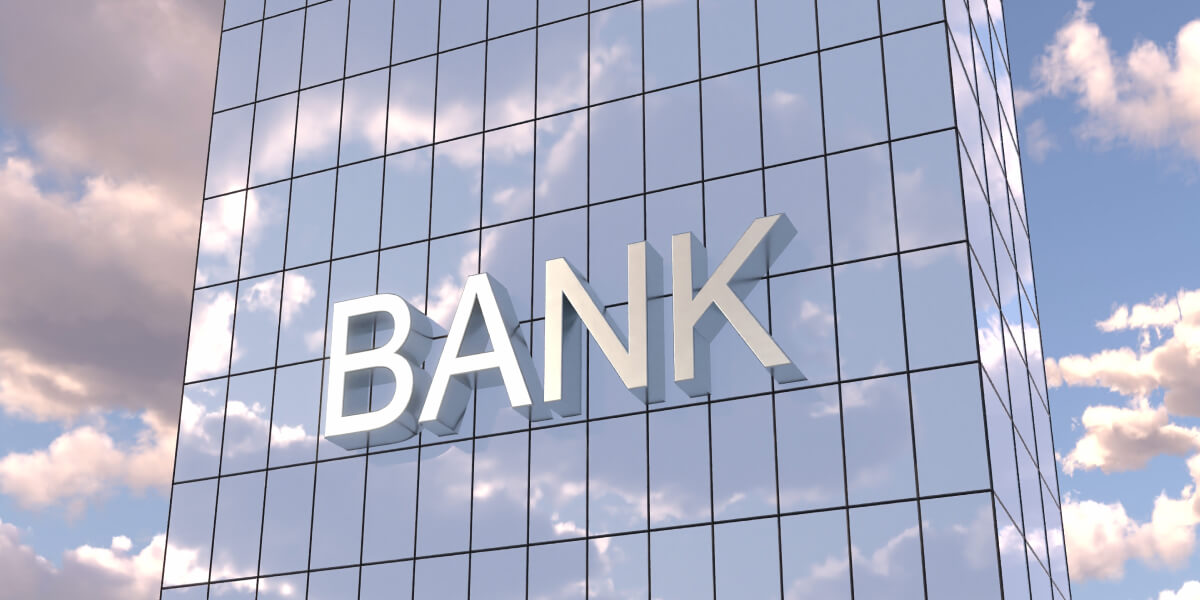 A modern building with a large "BANK" sign reflecting the sky.