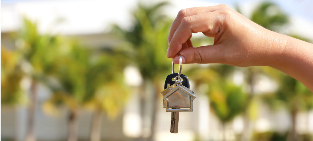 Close-up of a hand holding house keys with a blurred background of greenery, symbolizing homeownership.