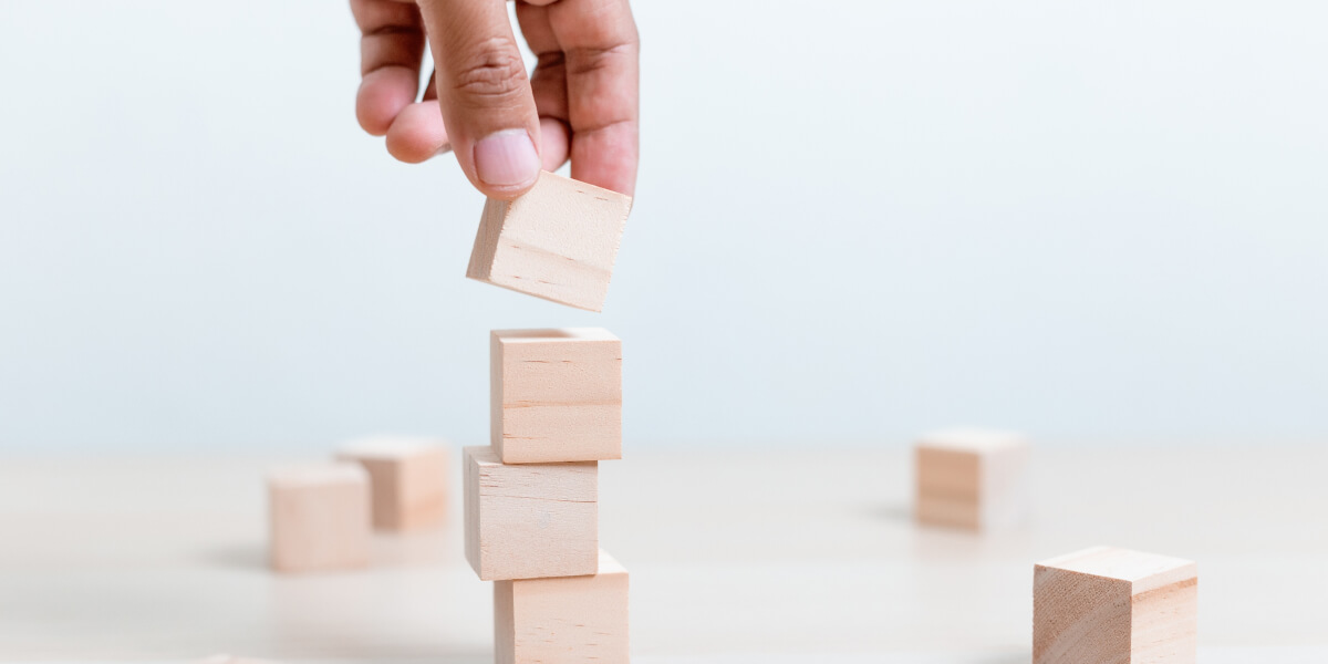 A hand placing a wooden block on top of other wooden blocks, symbolizing growth and progress in a business or investment context.