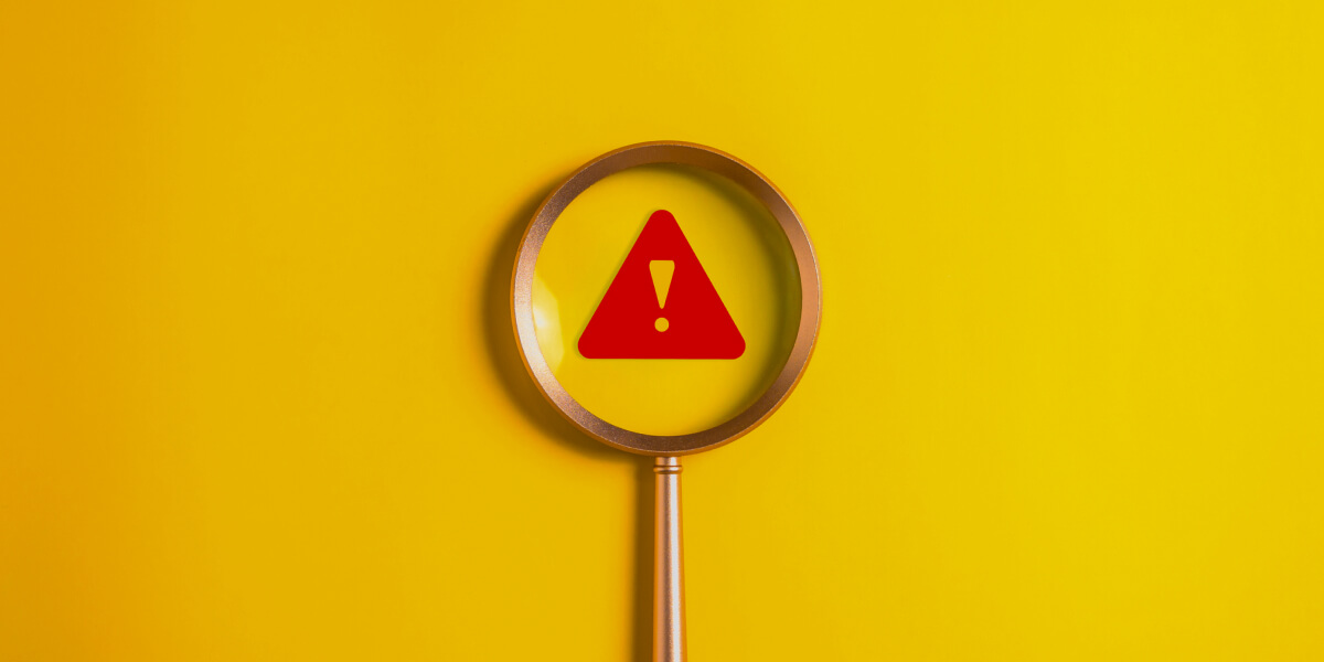 A magnifying glass highlighting a red warning symbol on a yellow background.