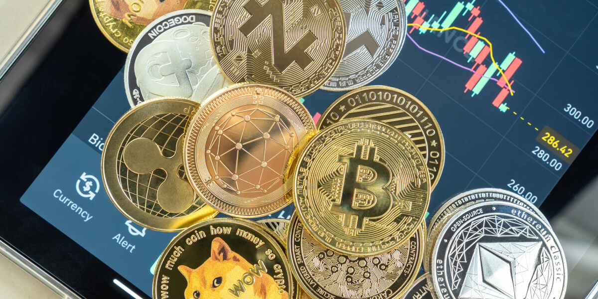 A collection of various cryptocurrency coins, including Bitcoin, Litecoin, and Ripple, placed on a smartphone screen displaying a trading app.
