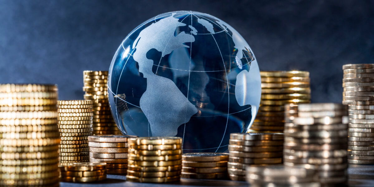 A reflective globe with a stack of gold coins beside it, symbolizing global finance and investment.