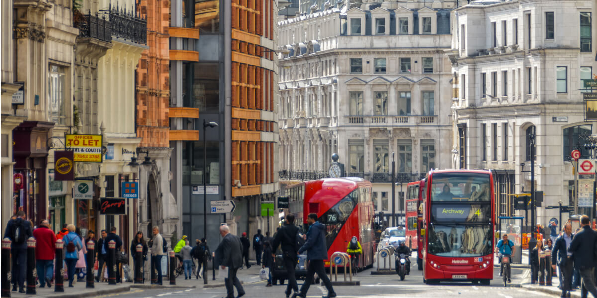A bustling London street lined with classic and modern buildings, shops, and a red double-decker bus.