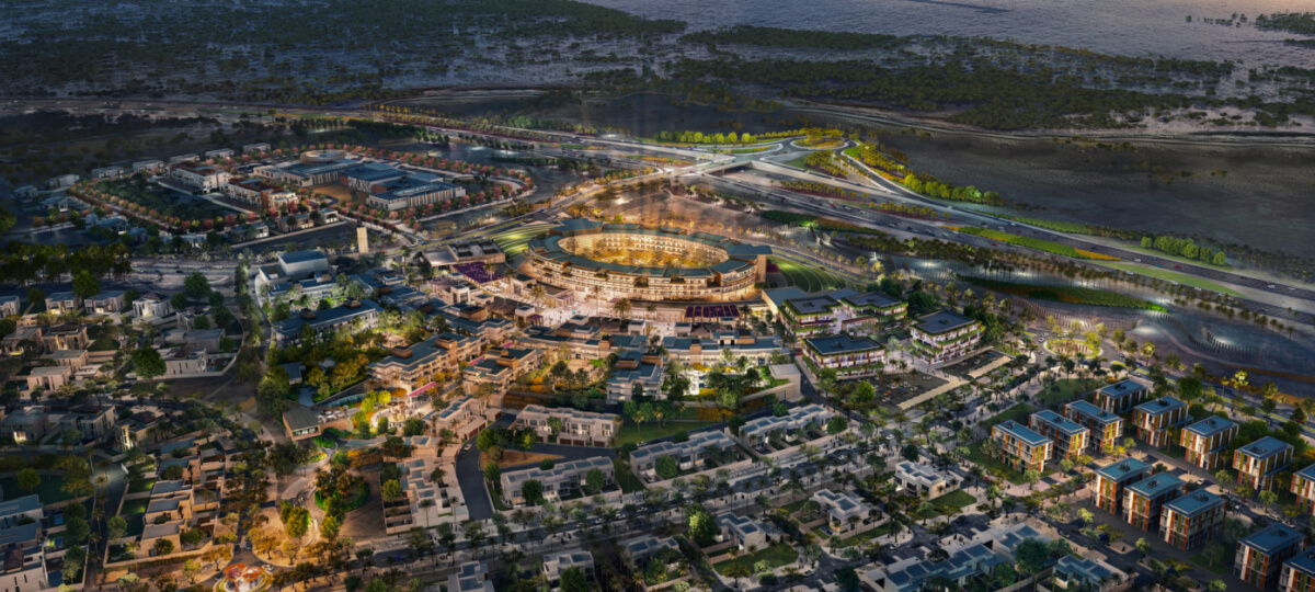 Aerial night view of a large master-planned community in Dubai, centered around a brightly lit circular arena with surrounding villas and amenities.