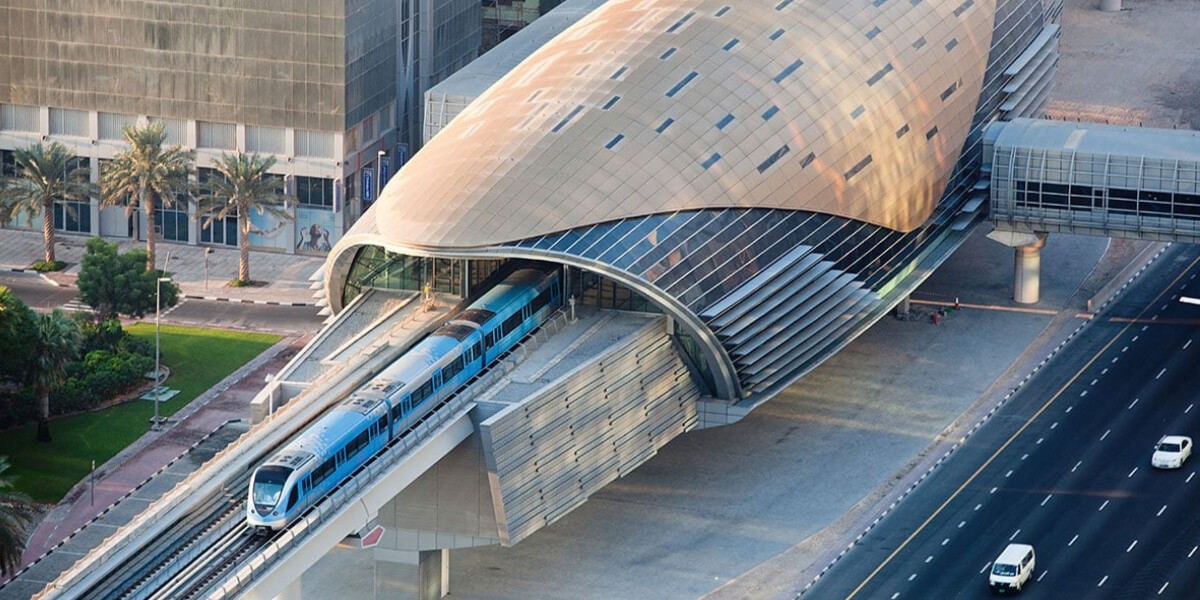 Dubai Metro station with a futuristic curved roof design, featuring a metro train arriving at the platform.