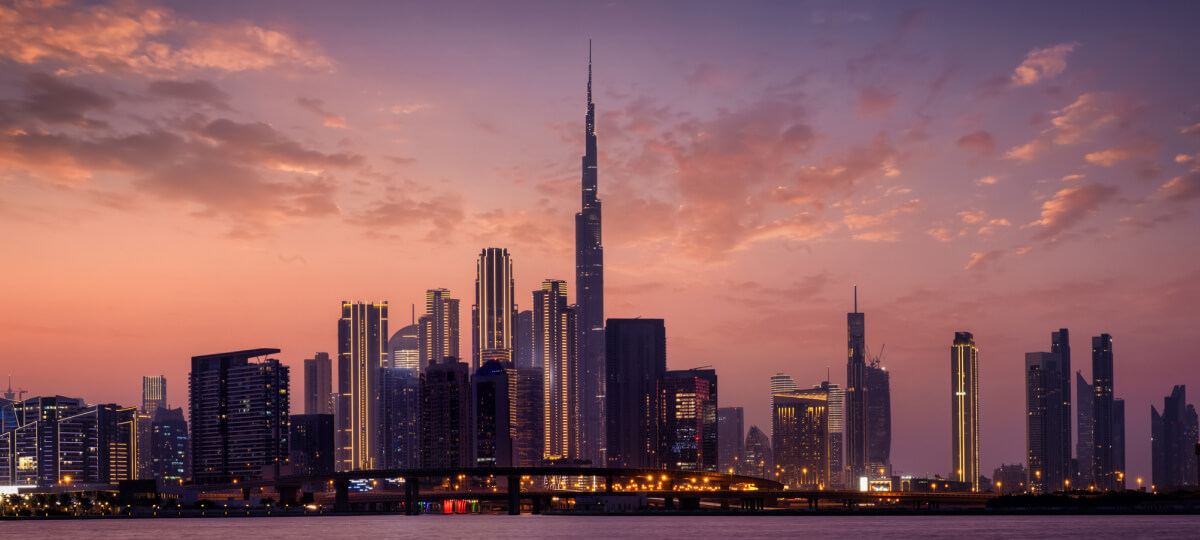 Burj Khalifa at dusk with lit-up skyline, under a vibrant purple-orange sky.