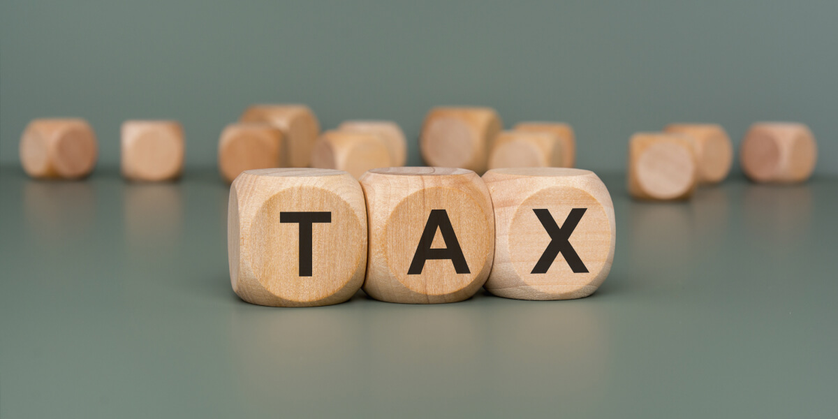 Three wooden cubes spelling “TAX” against a muted green background.