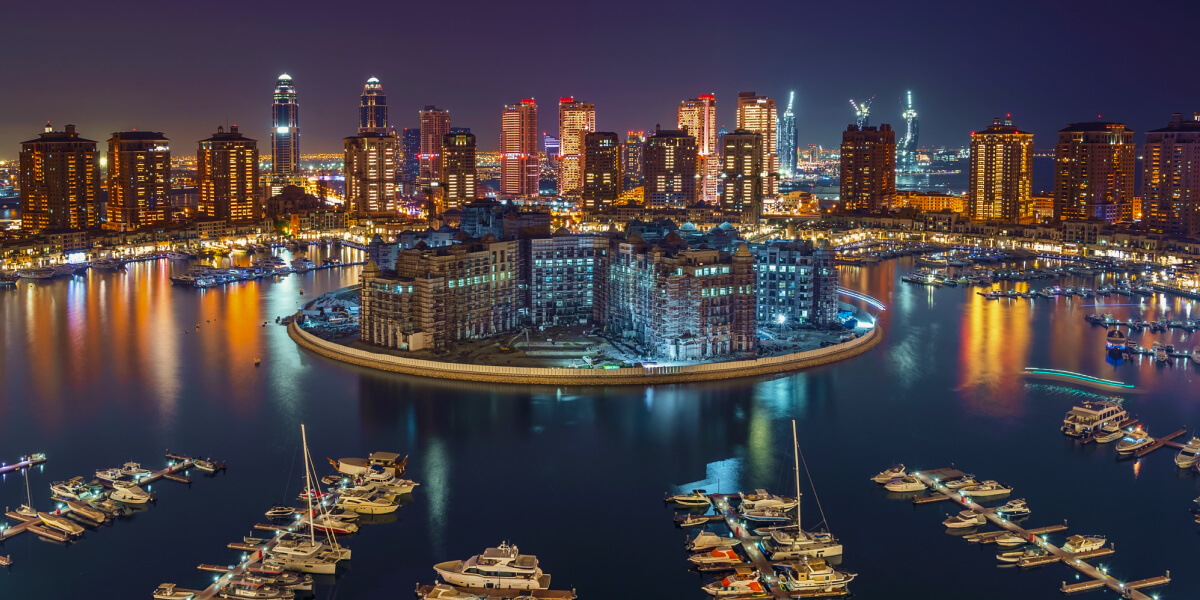 Night view of The Pearl-Qatar with lit-up skyscrapers and a marina reflecting city lights.
