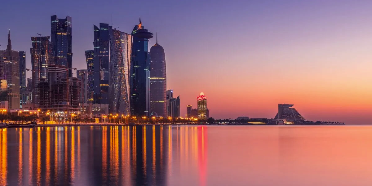 Twilight cityscape of Doha's West Bay with modern high-rise towers reflecting on the waterfront.