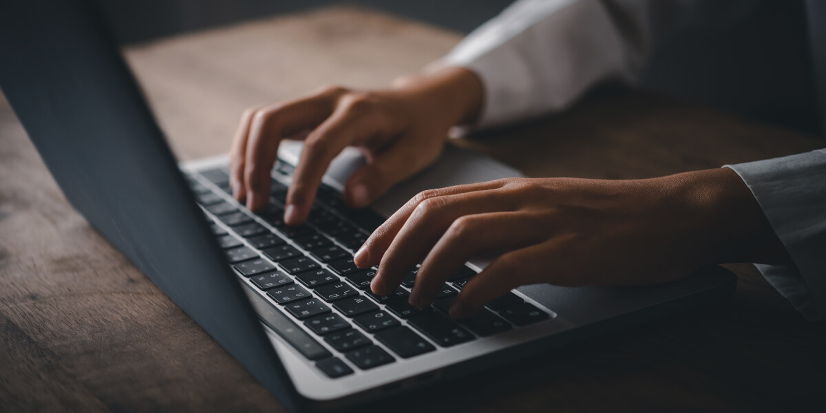 Close-up of hands typing on a laptop keyboard placed on a wooden desk.