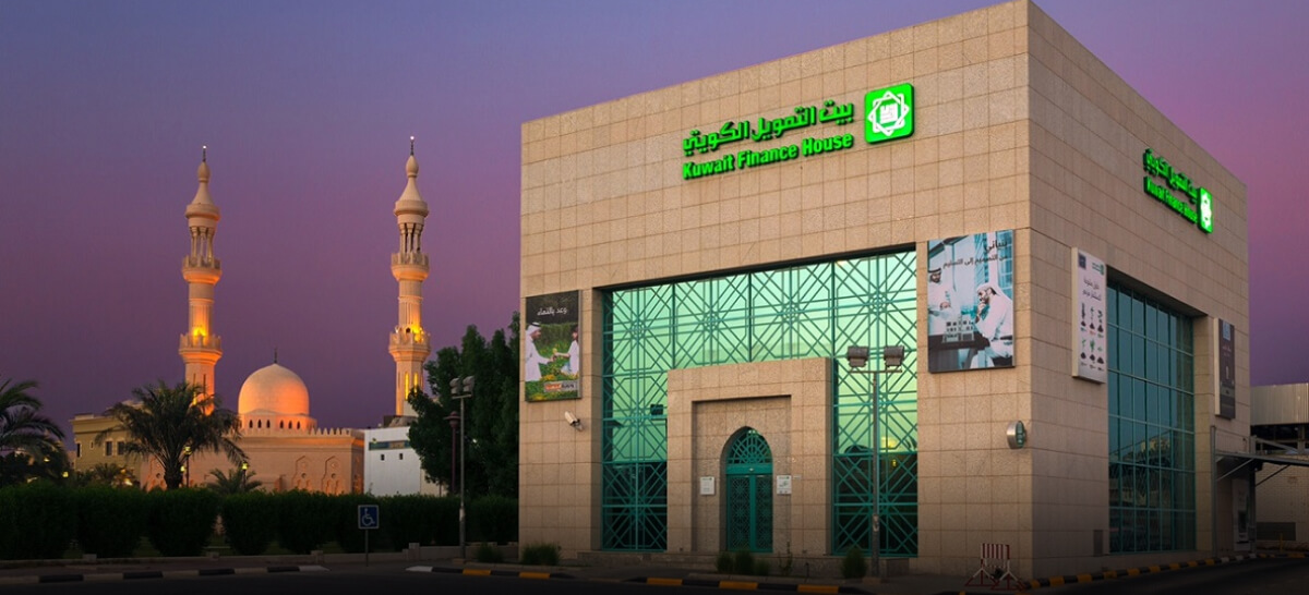 A mosque with lit domes and minarets stands next to a modern glass building at dusk.