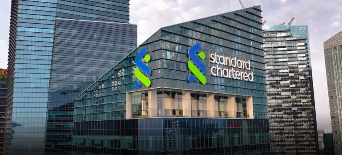 Exterior view of a glass-fronted Standard Chartered Bank building with its logo prominently displayed.