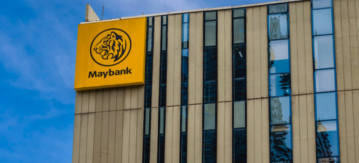 Maybank's logo with a tiger icon is displayed on a yellow sign attached to a high-rise office building.