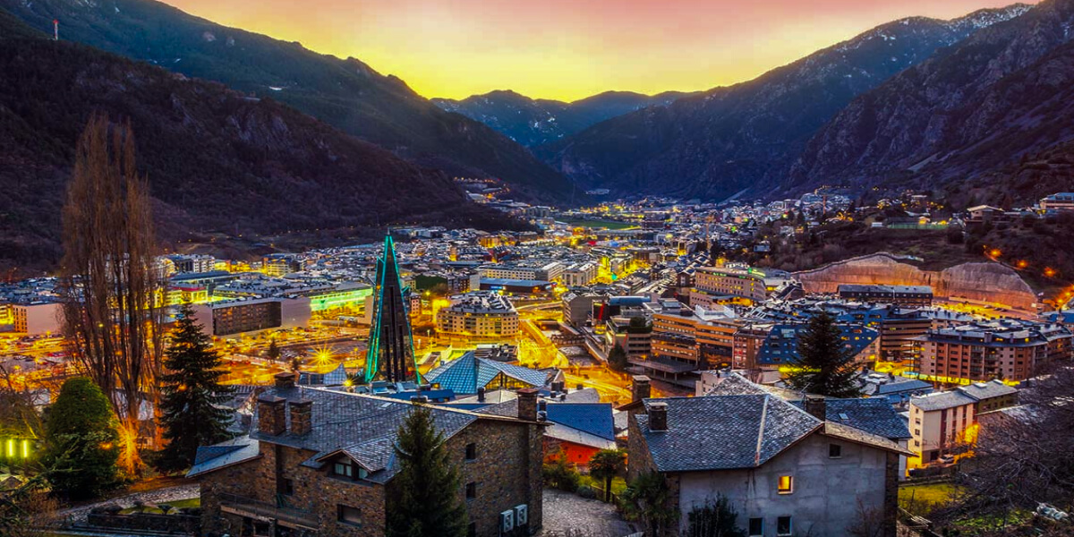 A glowing Andorran city nestled in the Pyrenees mountains during a vibrant sunset.