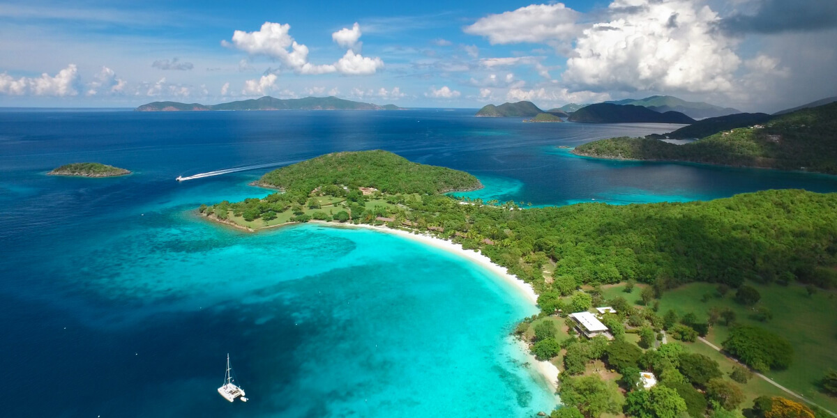A lush green island surrounded by crystal-clear turquoise waters and small boats.