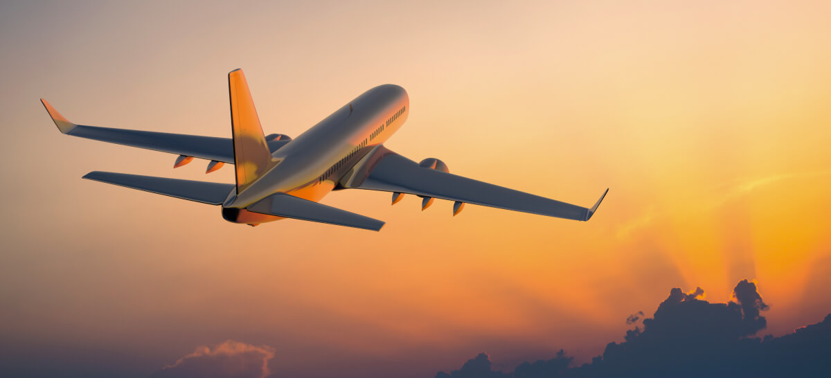 A passenger jet flies into the orange-lit sky during sunset.